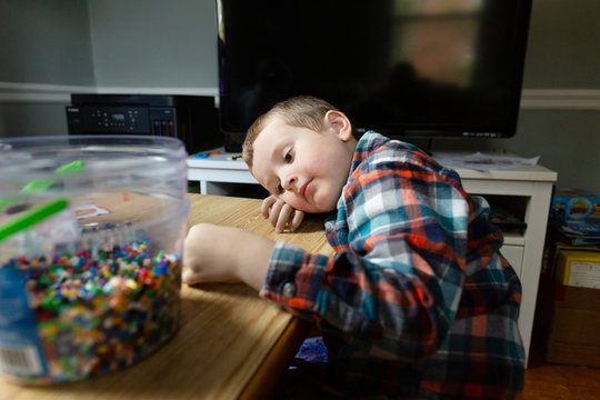 Preschool age boy quietly lays head on table while doing craft project