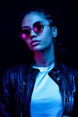 portrait of an African American young woman in sunglasses isolated on a black background in neon...