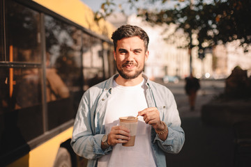 Happy man holding cup of coffee while standing on street during summer