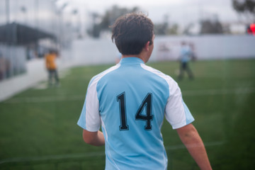 Teenage boy playing indoor soccer wearing light blue jersey number 14