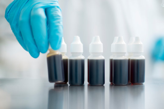 Blue glove hand picking up a vile with dark liquid