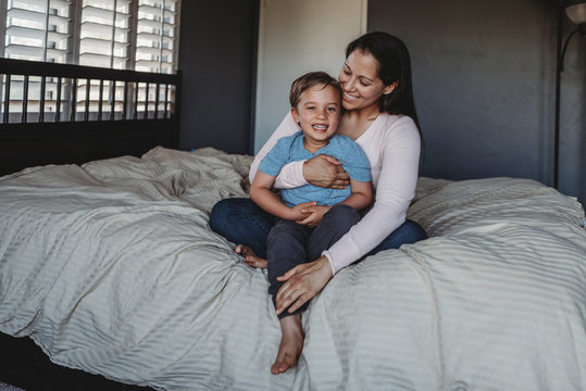 Smiling mom holding happy 5 yr old son on comforter near window