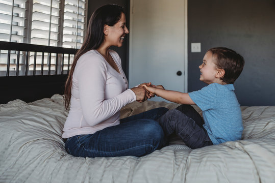 5 yr old boy and mid-30?s mom with long dark hair laughing on bed