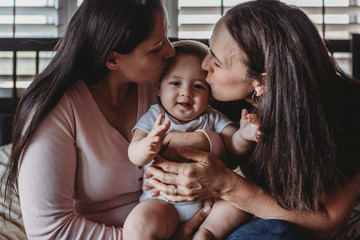 Loving moms holding smiling baby with outstretched arms