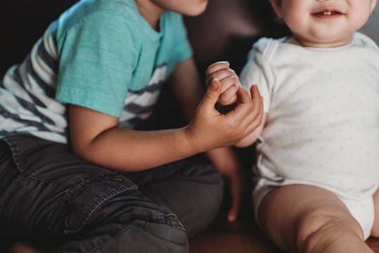Big brother holding hand of smiling baby sister in polkadot Onesie