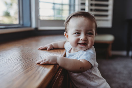 Smiling baby with two teeth standing by window seat
