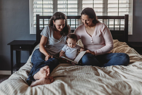 Same sex parents reading in bed with 8 mo old daughter