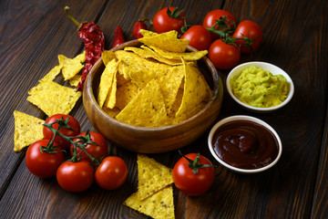 nachos in a wooden bowl and sauces on a wooden table