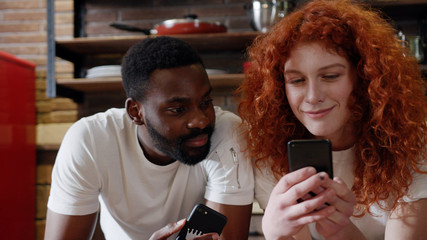 Close up african American man eat apple with curly red woman use their smart phone couple happy smile talk at home at kitchen girlfriend internet browsing technology together date shopping slow motion