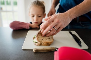 father making his kids packed lunches for school whilst daughter looks