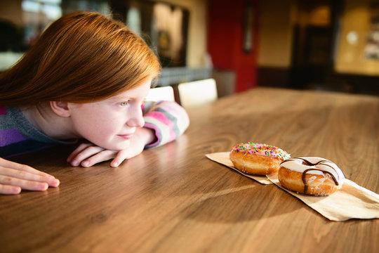 Young Red Haired Girl Looking Longingly at Two Delicious Doughnuts