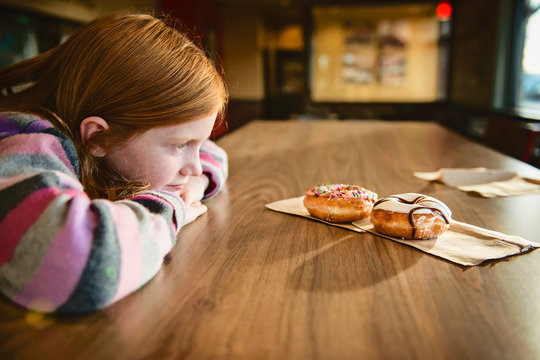 Young Red Haired Girl Looking Longingly at Delicious Doughnuts