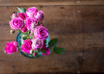 Hot pink miniature roses in a blue glass vase on dark vintage table.