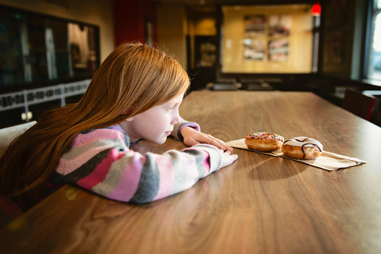 Young Red Haired Girl Looking Longingly at Delicious Doughnuts
