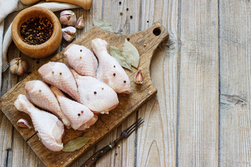 raw chicken legs on a wooden board on a table with seasonings for cooking