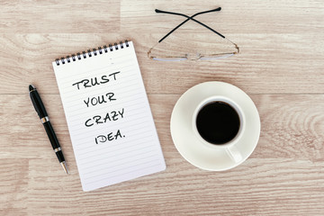 Inspirational and motivational - Trust your crazy idea text on note pad on top of wood desk
