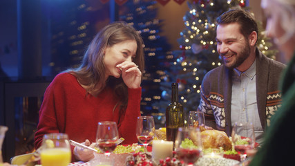 Attractive cheerful caucasian couple of man and woman sitting and laughing at dining table celebrating Christmas holiday dinner with friends.