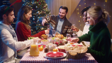 Caucasian smiling happy man host pouring wine into glasses treating his friends guests welcoming celebrating Christmas dinner and holidays together.