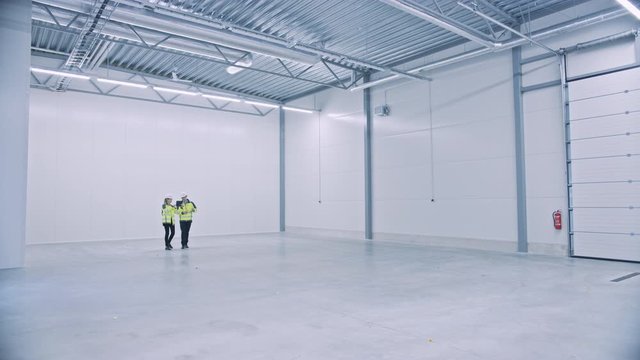 Industry 4.0 Modern Factory: Two Engineers Use Digital Tablet Computer with Augmented Reality Software Visualizing of Manufacturing Plant Room Mapping, Factory Layout. Illustrative Mock-up Concept