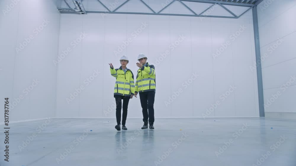 Aufkleber two engineers talking, walking across empty factory floor, inspecting, planning where all the machin