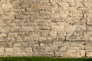 Old fortress wall of gray from stone blocks. At the bottom there is a strip of land covered with green grass. Background. Texture.