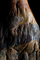 The art of Spanish Iberian ham. Whole leg with artistic look on a black background.