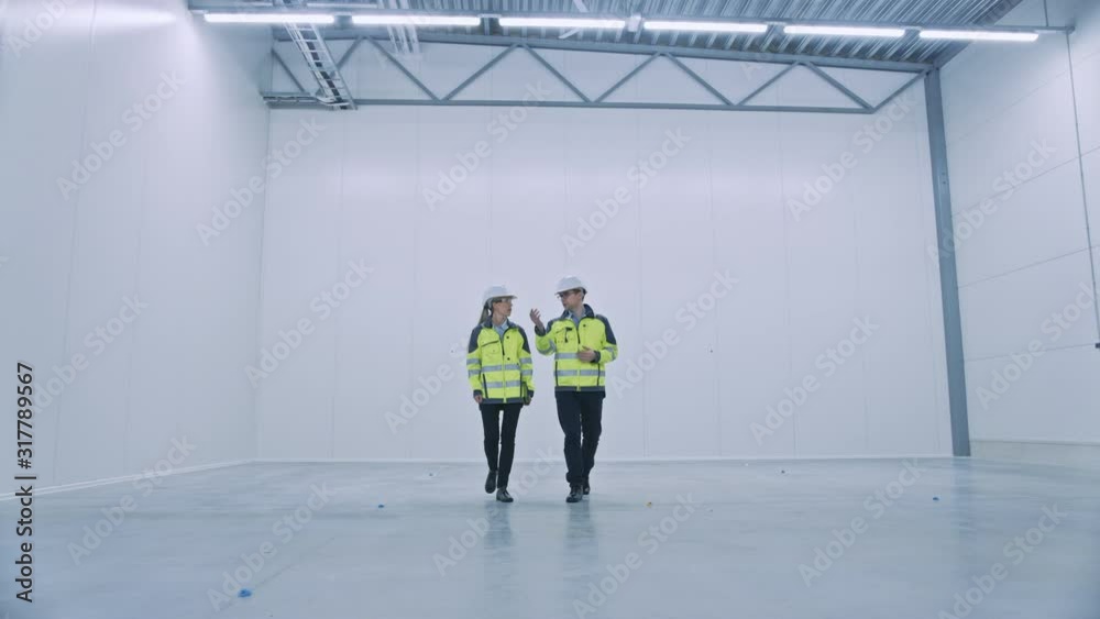 Aufkleber Two Engineers Talking, Walking Across Empty Factory Floor, inspecting, Planning Where All the Machinery Would go. Professionals Industrial Designers Strategizing about New Manufacturing Plant Design