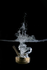  Singing bowl, Tibetan, plunging into water. On black background.