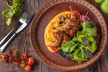 Baked quails with potatoes served with saffron sauce and green salad, a restaurant dish, Close up, Horizontal orientation