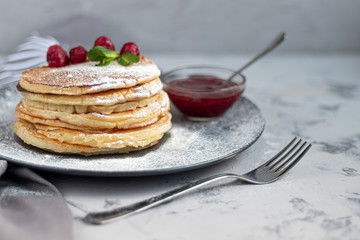 A stack of delicious pancakes with raspberries, blackberries and blueberries. On a light background. Sprinkled with icing sugar and decorated