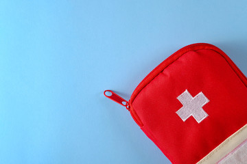 Closed red travel first aid kit pouch on the bright blue background. Photo with a copy space