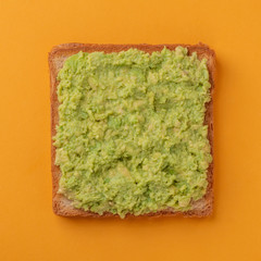 Top view on a toast with avocado on orange background
