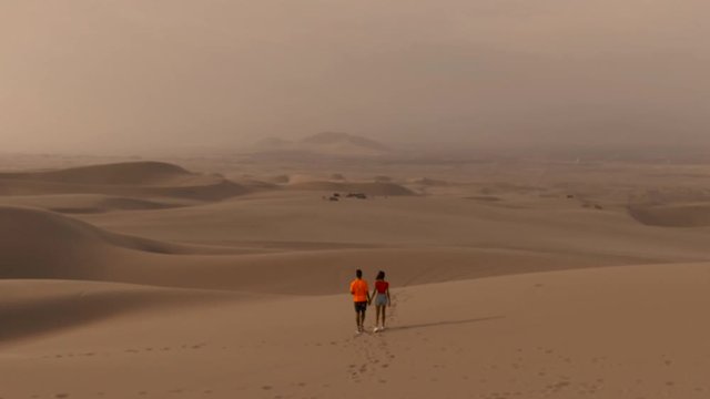 Sandy desert oasis lake. DRONE. Water in middle of hot sand desert. Romantic, holiday, couple, honeymoon, scenic shot, with sand and footprints. Tourism shot in Huacachina, Peru. Epic, dramatic shot.