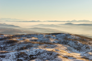 Golden hour view of misty mountain layers and vast, soft , frozen landscape covered with snow
