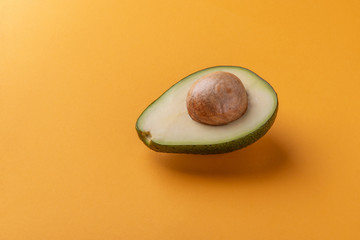 Avocado half with kernel on orange background. Tropical fruit