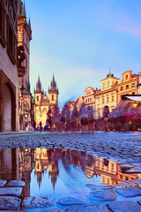 St Mary Tyn Church in Prague with reflection in a pool of water after Summer rain with tourists walking by towards Old Town Square. Prague, Czech Republic.