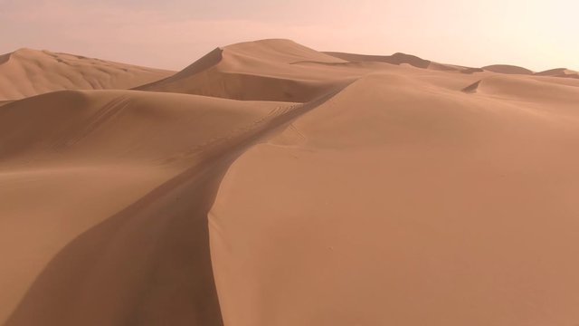 Sandy desert oasis lake. DRONE. Water in middle of hot sand desert. Romantic, holiday, couple, honeymoon, scenic shot, with sand and footprints. Tourism shot in Huacachina, Peru. Epic, dramatic shot. - Powered by Adobe