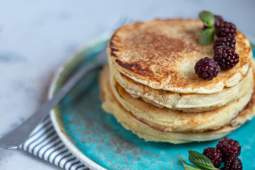 A stack of delicious pancakes with raspberries, blackberries and blueberries. On a light background. Sprinkled with icing sugar and decorated