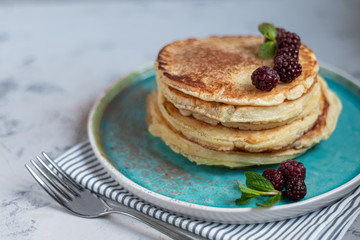 A stack of delicious pancakes with raspberries, blackberries and blueberries. On a light background. Sprinkled with icing sugar and decorated