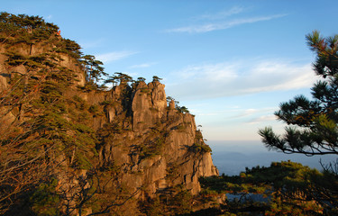 Huangshan Mountain in Anhui Province, China. View at sunrise near Stone Monkey Watching the Sea viewpoint with rocky cliffs and pine trees. Scenic view of peaks and trees on Huangshan Mountain, China.