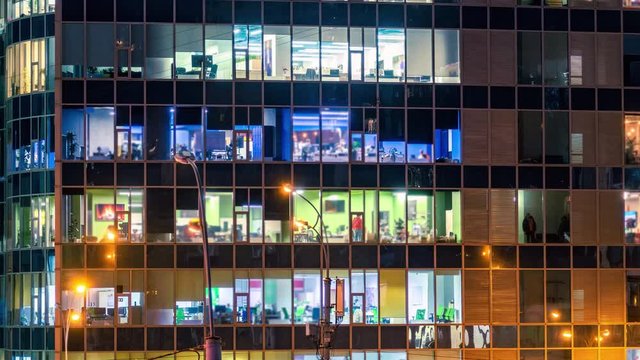 Office building exterior at night with a lot of white collars inside working overtime. Time lapse. Zoom effect