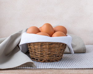 Brown fresh raw eggs lie on a white napkin in a small rough rustic basket.