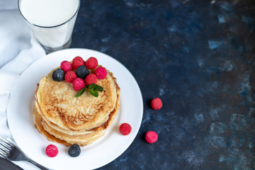 A stack of delicious pancakes with raspberries, blackberries and blueberries. On a dark stone background. Sprinkled with icing sugar and decorated