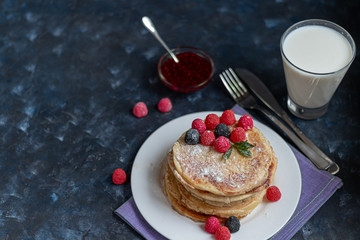 A stack of delicious pancakes with raspberries, blackberries and blueberries. On a dark stone background. Sprinkled with icing sugar and decorated