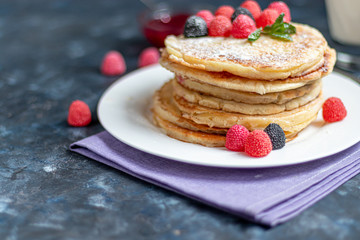 A stack of delicious pancakes with raspberries, blackberries and blueberries. On a dark stone background. Sprinkled with icing sugar and decorated