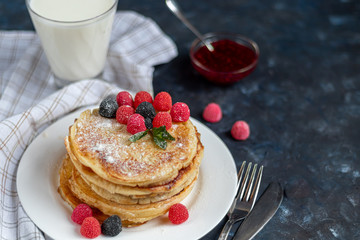 A stack of delicious pancakes with raspberries, blackberries and blueberries. On a dark stone background. Sprinkled with icing sugar and decorated