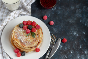 A stack of delicious pancakes with raspberries, blackberries and blueberries. On a dark stone background. Sprinkled with icing sugar and decorated