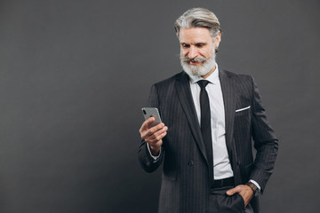 Business and fashionable bearded mature man in a gray suit talking on the phone and smile on the grey background.