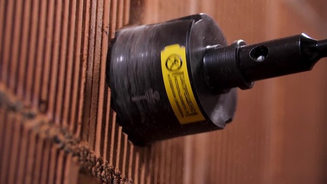 Close up of boring hole process in wall for electric outlet by power hammer drills tool. Stock footage. Making a hole inside red brick wall with a professional equipment.