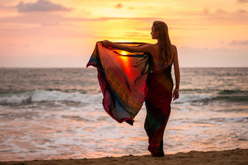 Beautiful young woman on the beach of the ocean at sunset